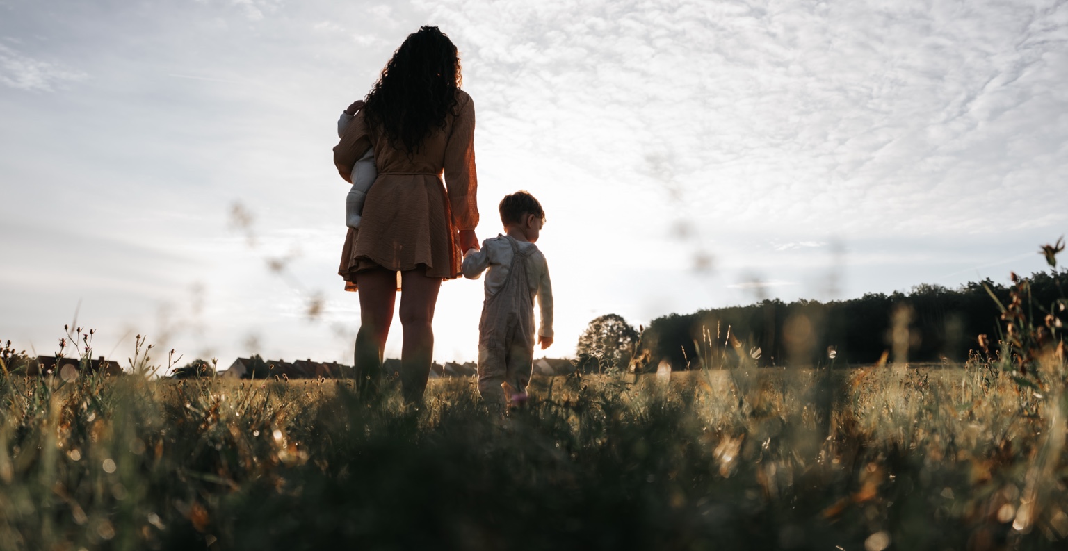Mutter geht mit ihren beiden Kindern durch eine Wiese
